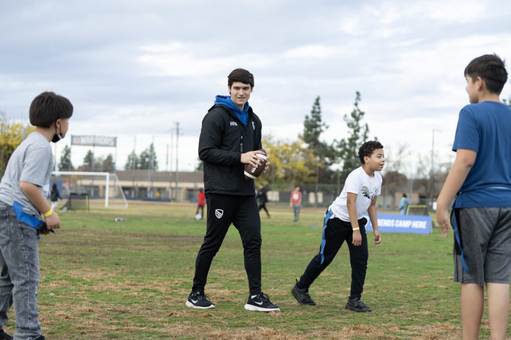 elop coach throwing a football to school aged kids